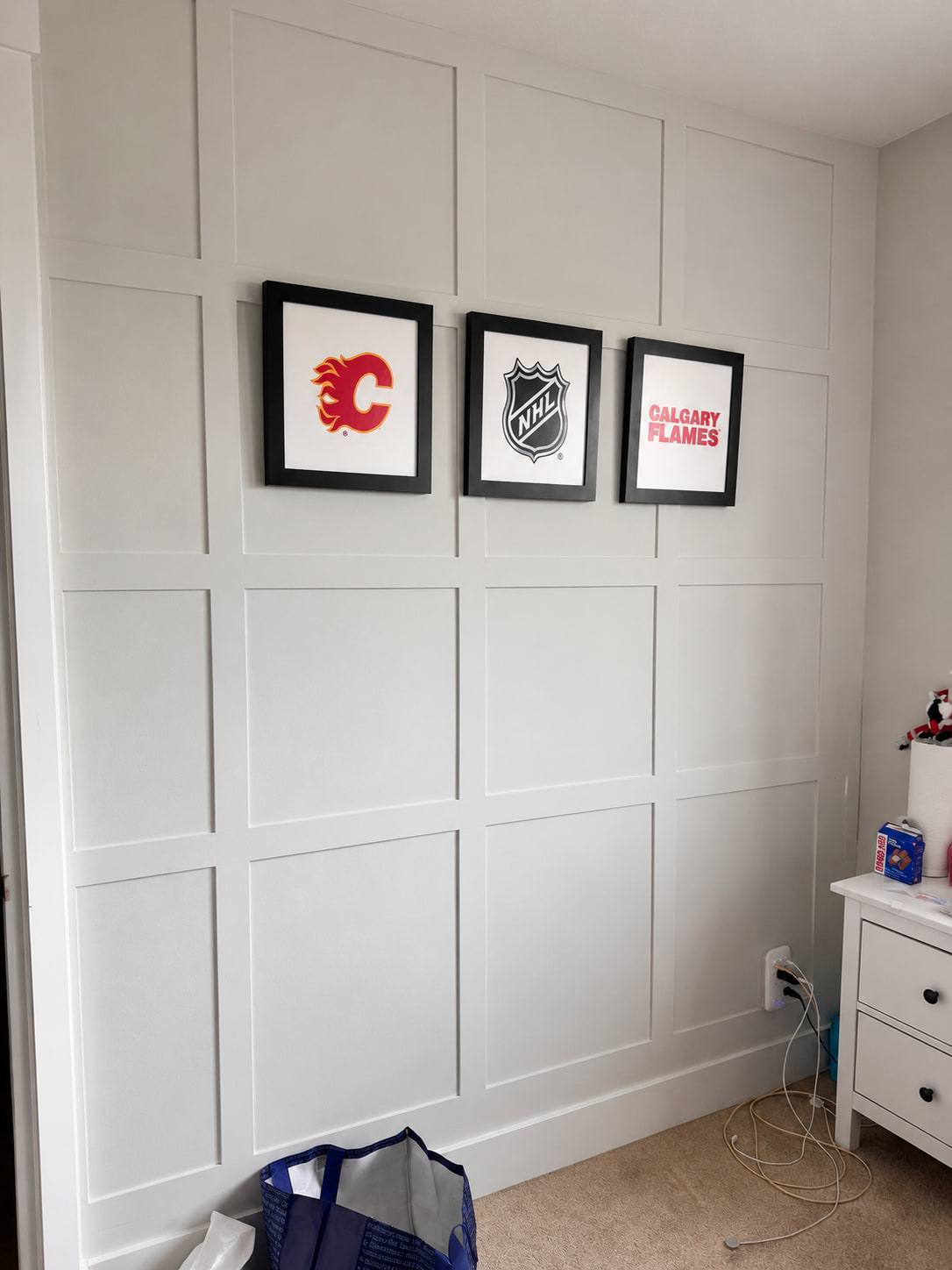White board-and-batten panel wall running floor to ceiling with three framed hockey prints hung on it