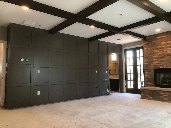Large wall covered in dark-painted grid panels under a dark beamed ceiling, beside a brick fireplace