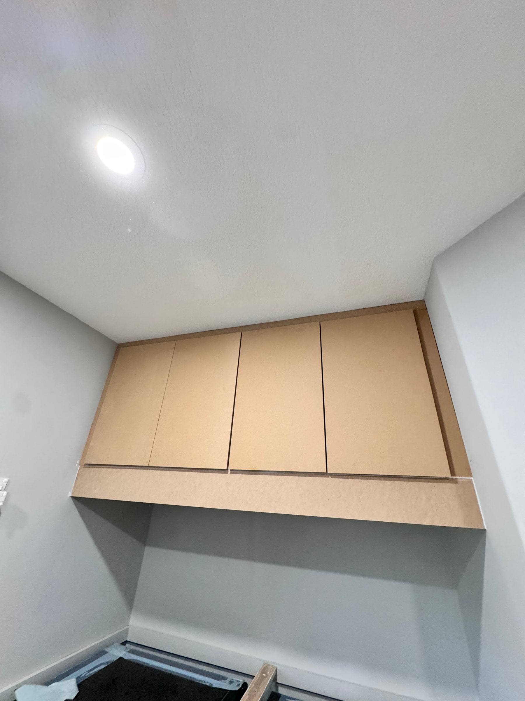 Tapered range hood cover in raw MDF mounted to the wall above the range location