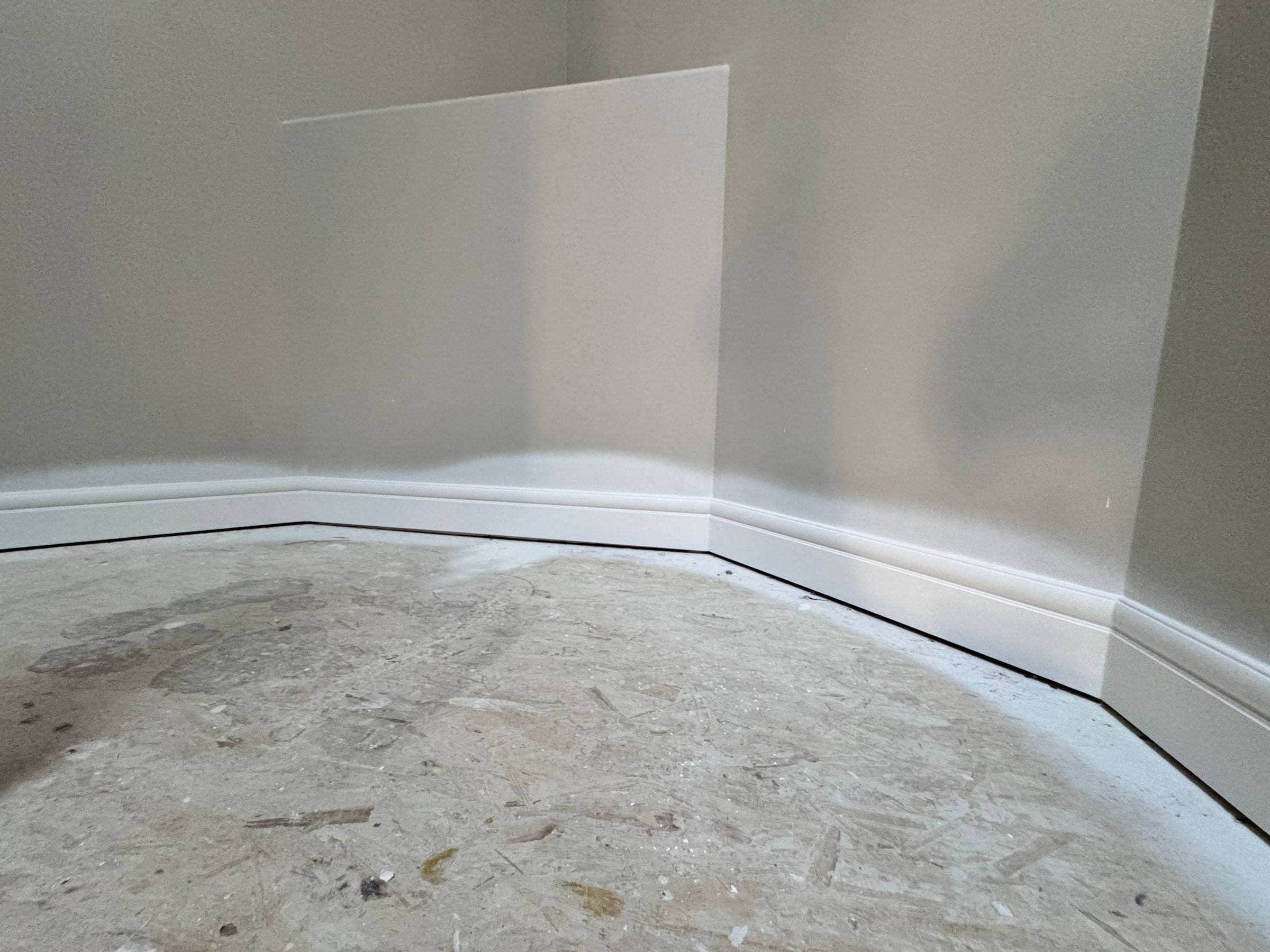 Tall white baseboard following a curved and angled wall before flooring